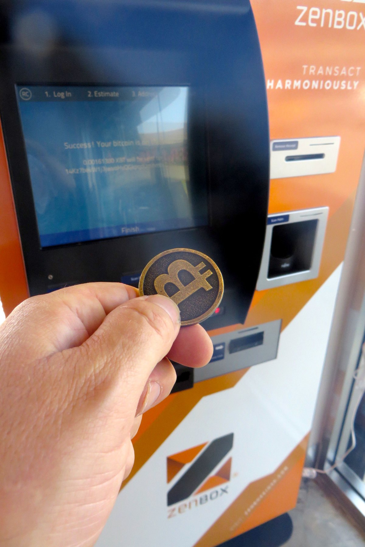 A person holds a coin with a B in front of an orange machine.